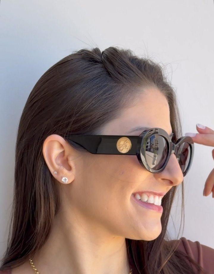 Cliente de perfil com óculos de sol oval preto com detalhe dourado na haste